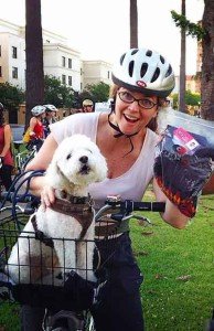 A woman on abike with her dog in a basket in front of her