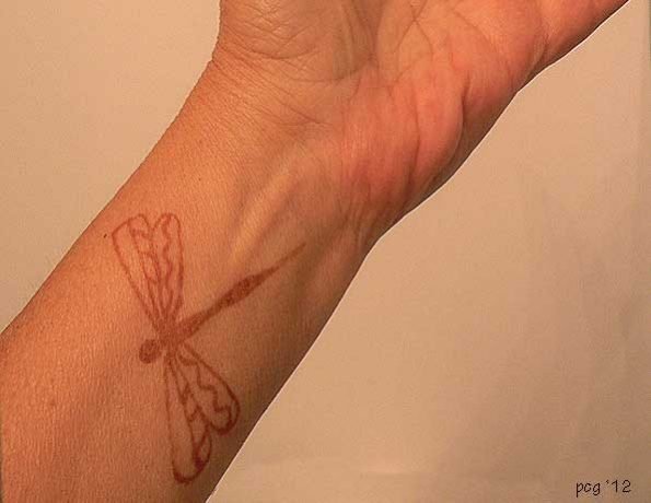 A wrist with a red dragonfly tattoo