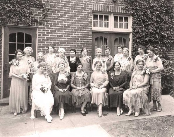 A black and white photo of a group of women gathered in front of a building in the 30s