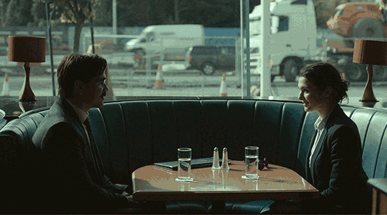 A man and a woman sitting by a window with cars moving outside