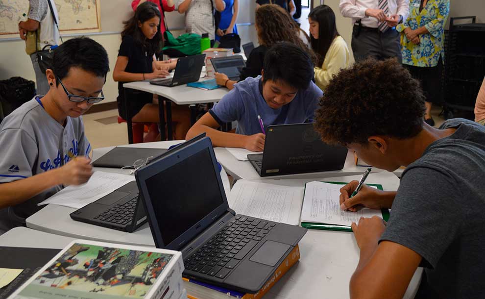 Students working on desks with laptops and pen