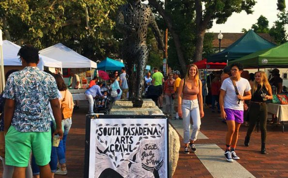 a man and woman pass a sign that advertises the Arts Crawl