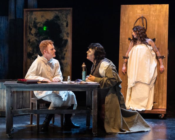A woman in a white sack is stuck on the wall and Frankenstein is wearing a dark robe conversing with a man with a white robe