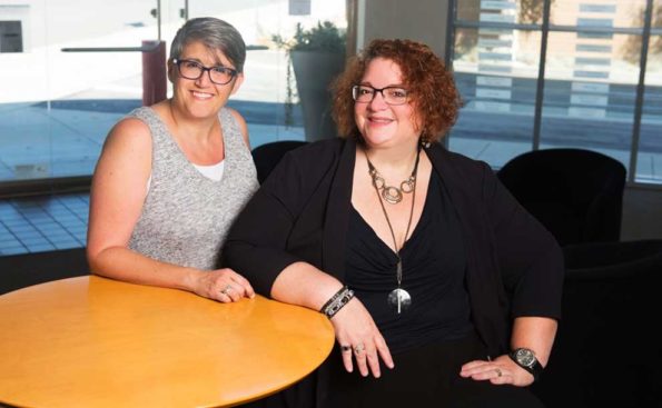 2 women, both in glasses, sitting in front of a table