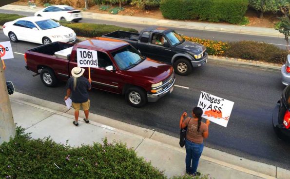 a woman with a sign that says "villages my ass" protests in front of cars stuck in traffic