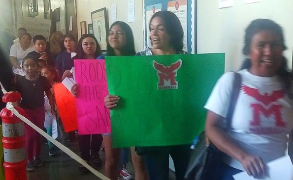 Parents and students protest holding signs depicting the emblem of their school