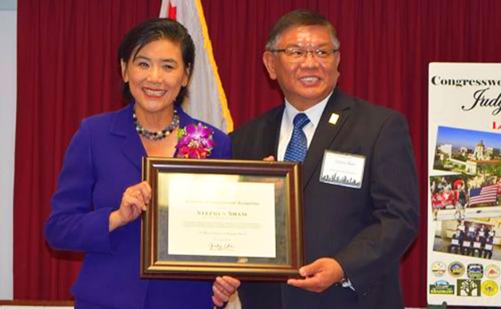A woman in blue dress holds a certficiate along with a man in a blue tie and a suit
