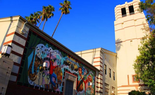a mural of disney characters and cartoons on a wall surrounded by a school tower and palm trees