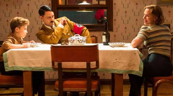 a man dressed as Hitler with a boy next to him and a mom on the other side of the dinner table