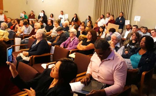 An Asian woman taking a photo of the council and people behind her holding signs