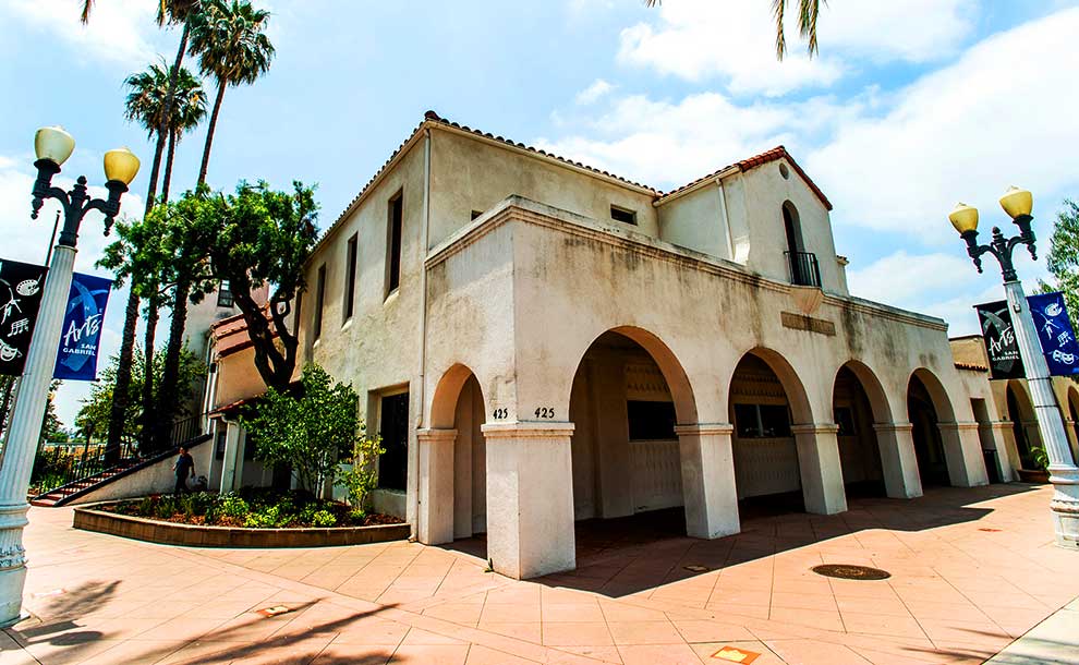 An old Spanish style building with trees and banners in front of it