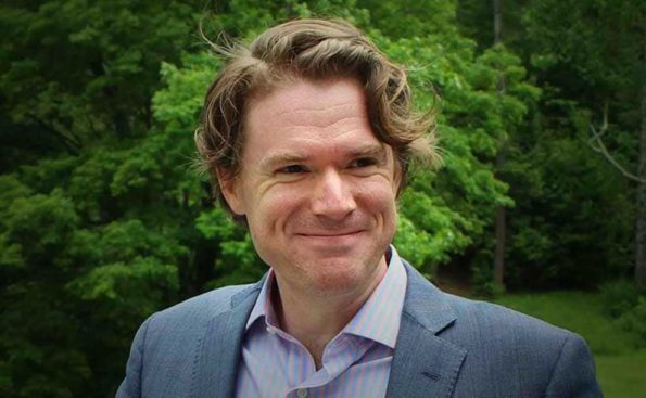 A white man in a blazer smiling at the camera