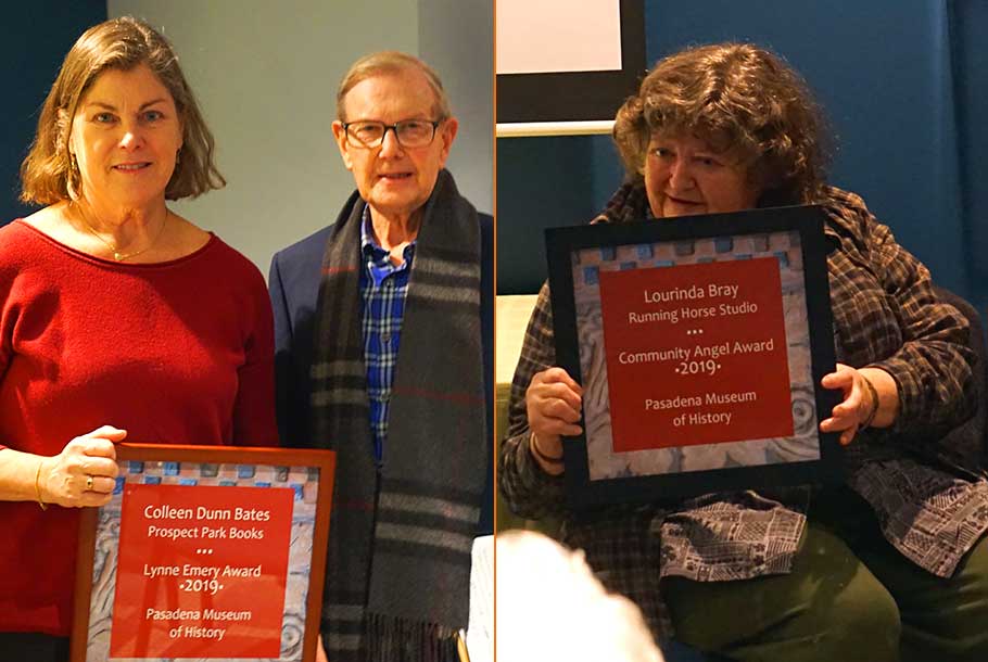 A woman in a red sweater stands near a man with glasses and another woman sitting, both holding a plague honoring them