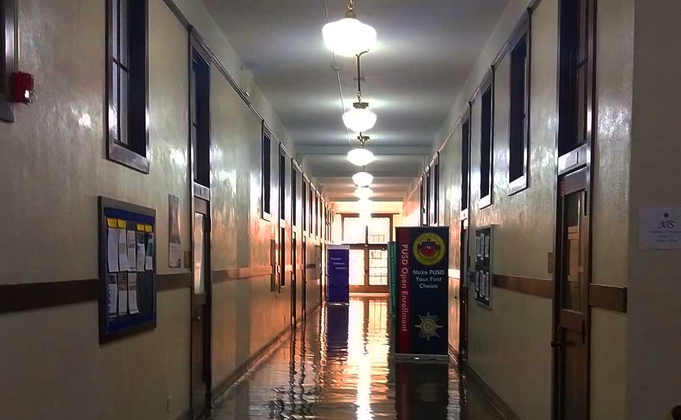A hallway with lighting fictures in the ceiling and a door with PUSD logo on it