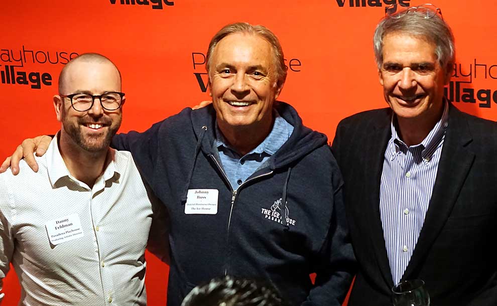 3 white men smile at the camera behind a sign announcing Passadena Village