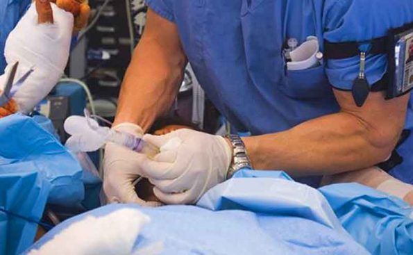 A person in blue scrubs and while gloves removes a tube