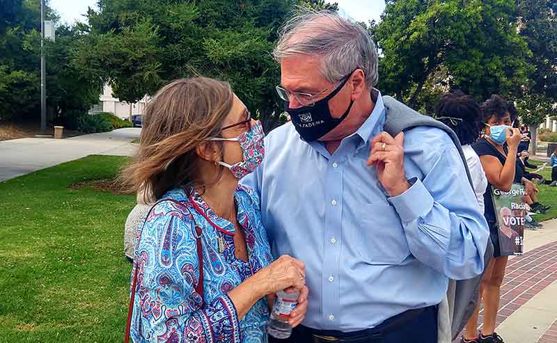 A white haired man with a woman next to him, both with masks