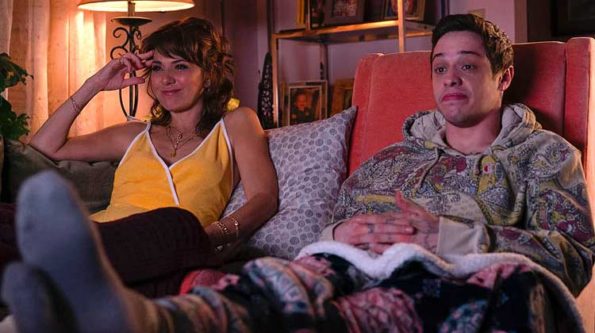 a woman in yellow blouse and a guy in shorts sittingon a sofa