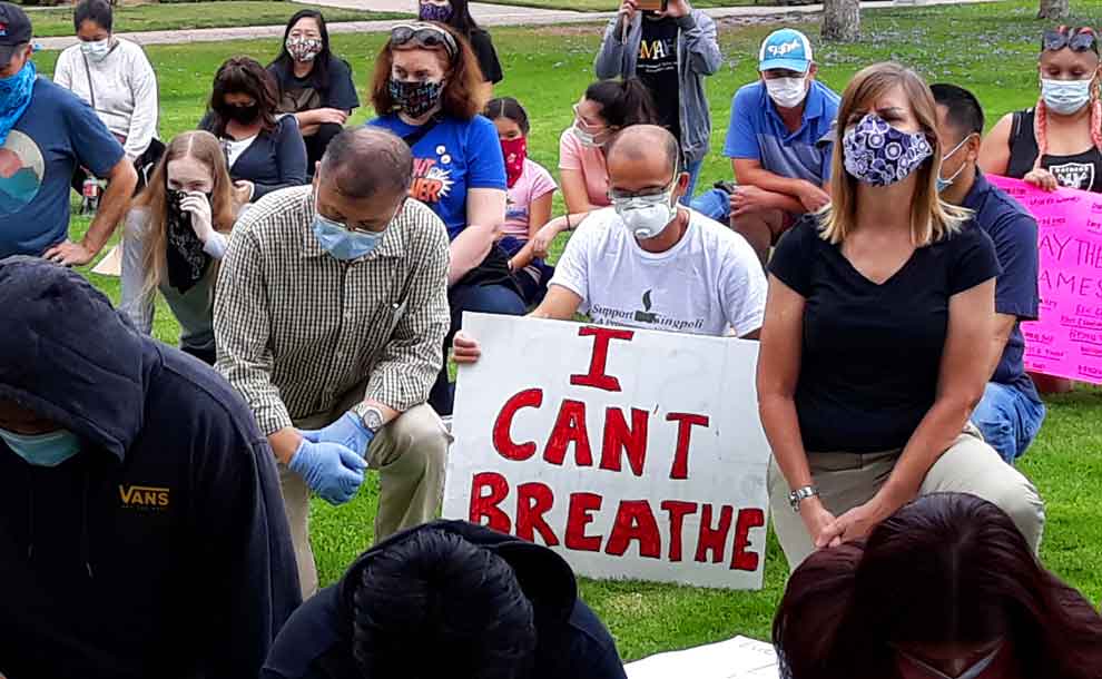 a man kneeling next to a sign that says" I can't breathe