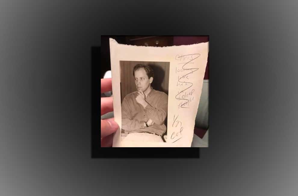 A hand in color is hodling a photo of a young man in black and white