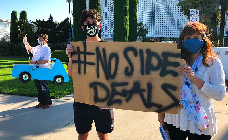 Two people holding a sign that says: No Side Deal