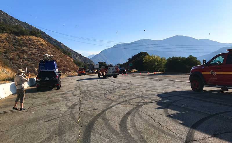 tv crew truck and police cars and someone taking a photo on a blocked highway