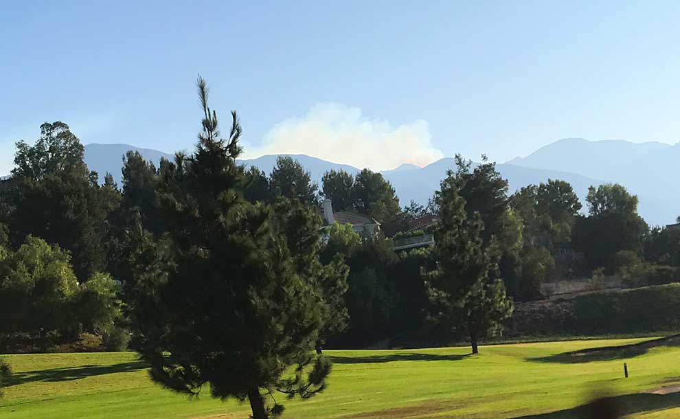 A vast green with hills and a plume of smoke behind them