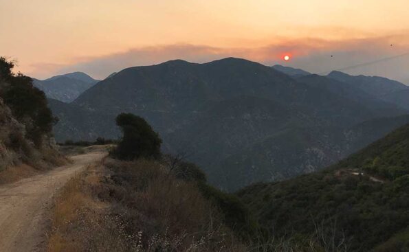 a trail to the left and hills. Sun is muted with dark orange colors