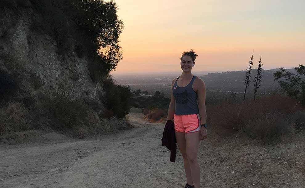 a woman in oink shorts and a tanktop posing on a hiking trail