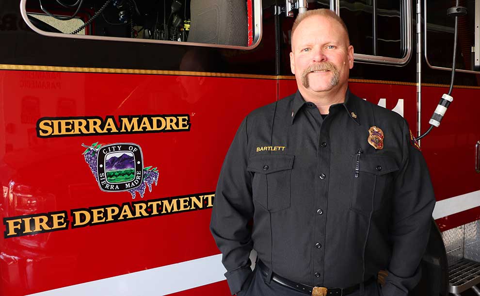 A white man with moustache in fire uniform standing in front of Fire Truck