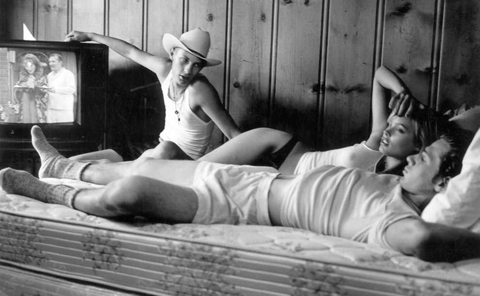 two men in bed with a woman watching TV