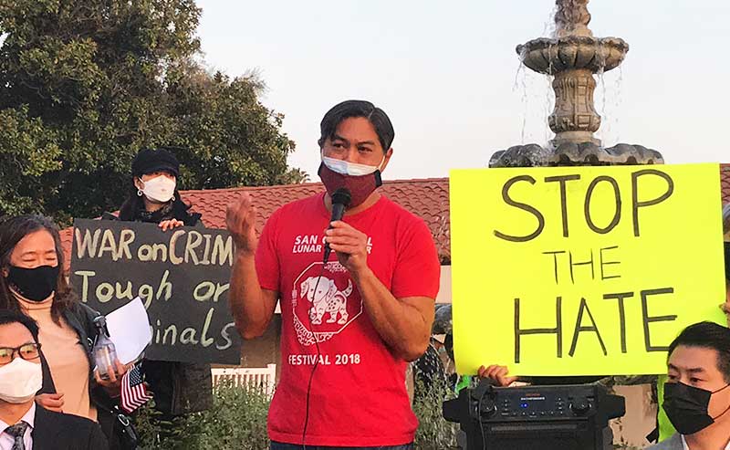 A man speaking to a crowd with signs denouncing racism