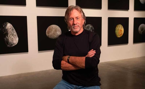 a man with glasses in front of framed photos of an exhibition