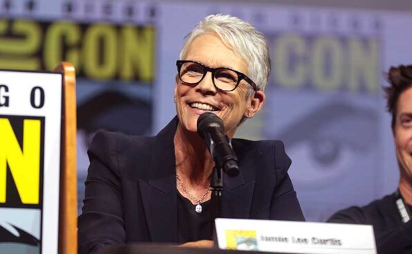 a woman with white hair and glasses talking on a microphone and smiling