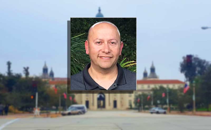 a bald man smiling in fromt of a building