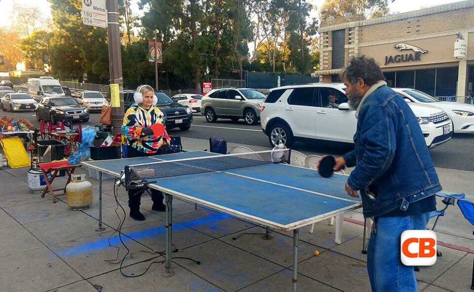 two people playing ping pong on the sidewalk