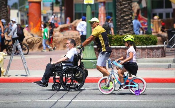A man on a wheelchair and a child on a bike behind him