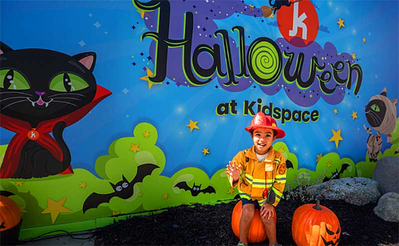a kid sitting on a pumpkin and behind him a giant mural of Halloween