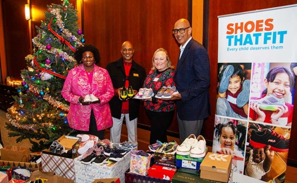 People holding brand new donated shoes next to a holiday tree