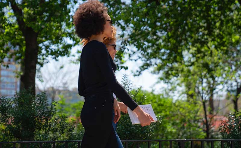 two women walking while holding a book