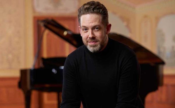 A man sitting besides a piano smiling