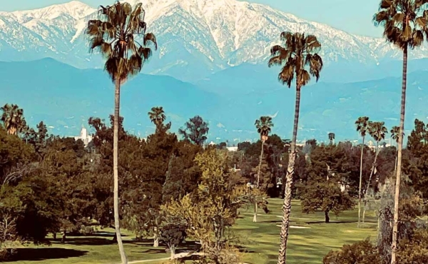 A panoramic view of a golf course with snow capped mountains in the background