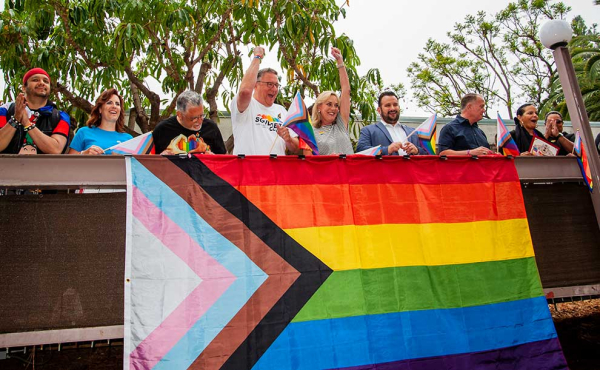 People waving and a Pride flag in front of them