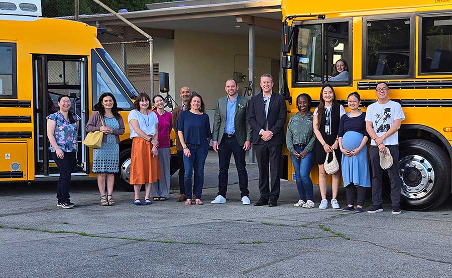 a group of people stand next to 2 buses
