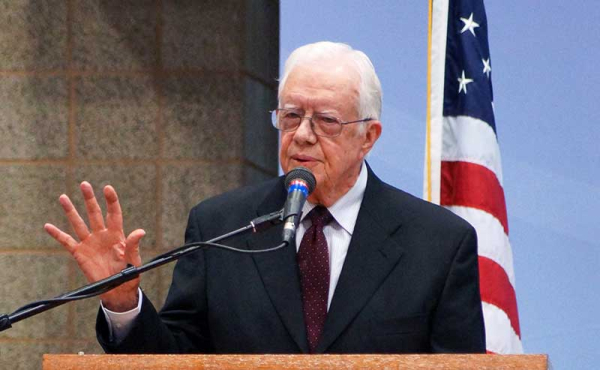 a man speaking with the US flag behind him