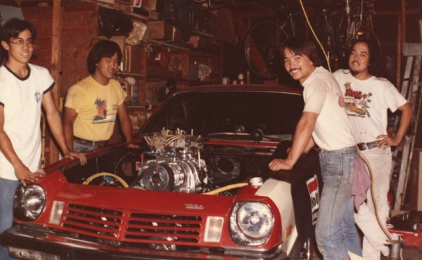 Four men gathered around a car with the hood popped open