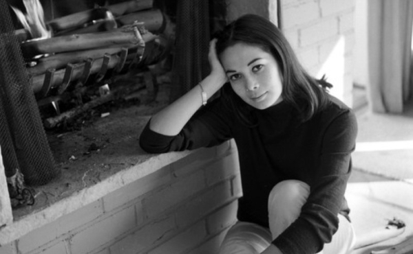 A black and white photo of a woman next to a fireplace