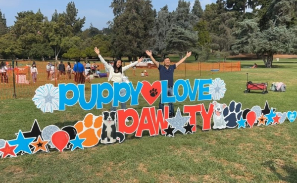 Two people posing next to a sign saying "Puppy Love Paw-ty"