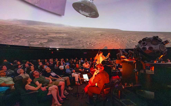 audience look upwards towards the ceiling while music an orchestra plays live music