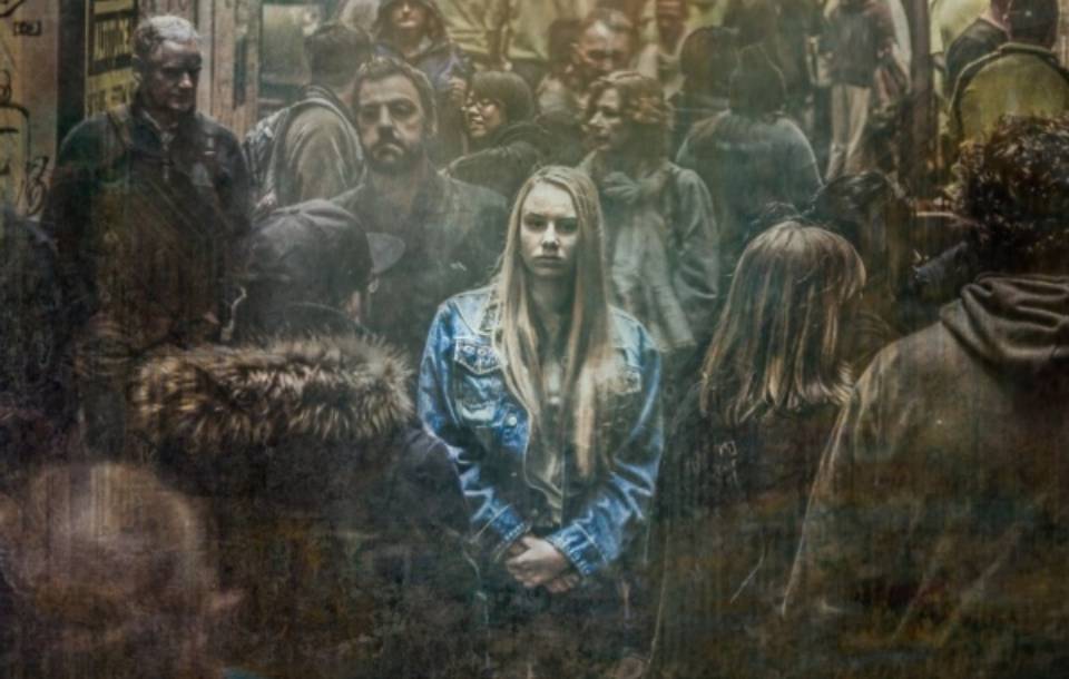 A woman wearing a blue jacket appears sad in a crowd.